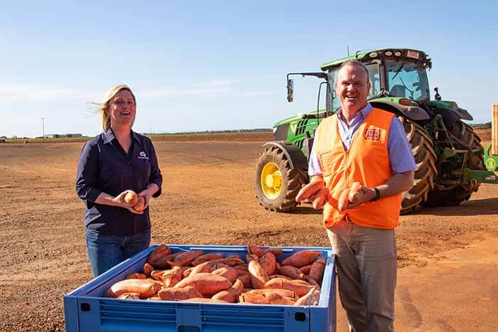 two people smiling with their sweet potato harvest