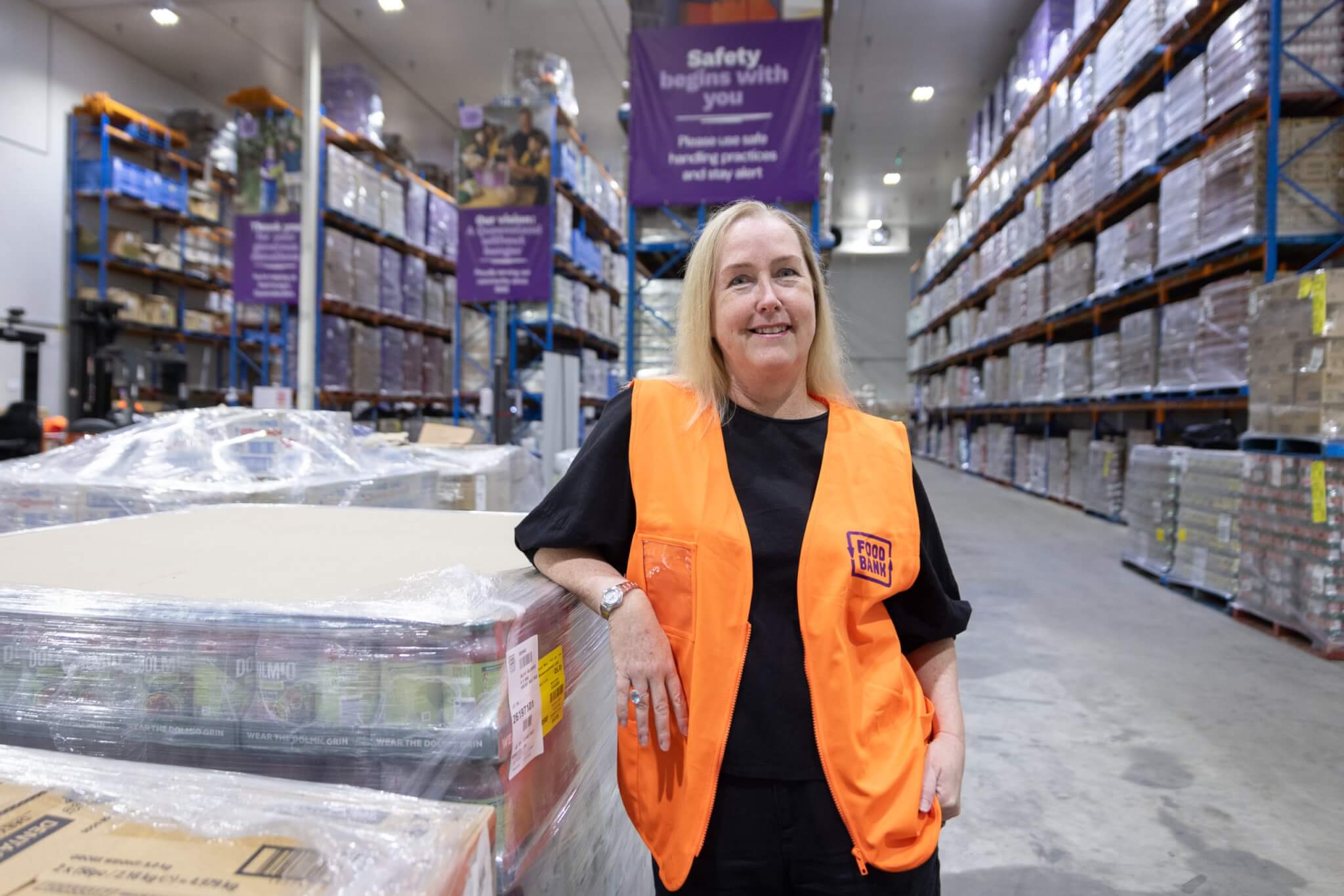 Foodbank Queensland Interim CEO in warehouse with sign showing alt=