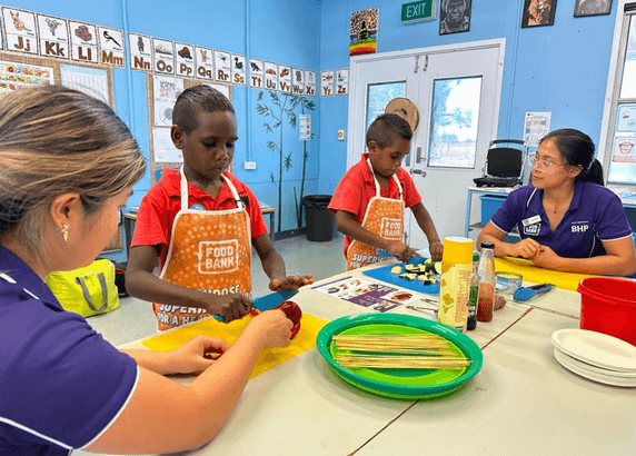 two foodbank staffs guiding children in cooking