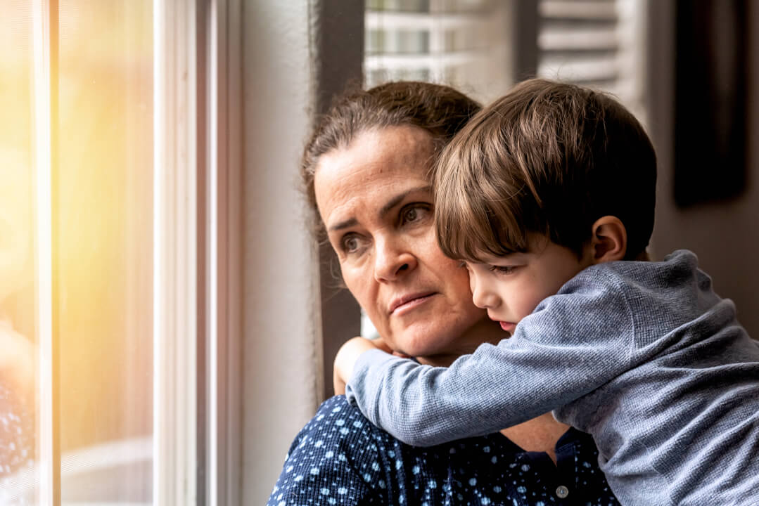Sad Unemployed mature woman holding her son in her arms looking through a window