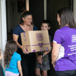 Mum and three children being handed a Foodbank hamper by a Foodbank staff member